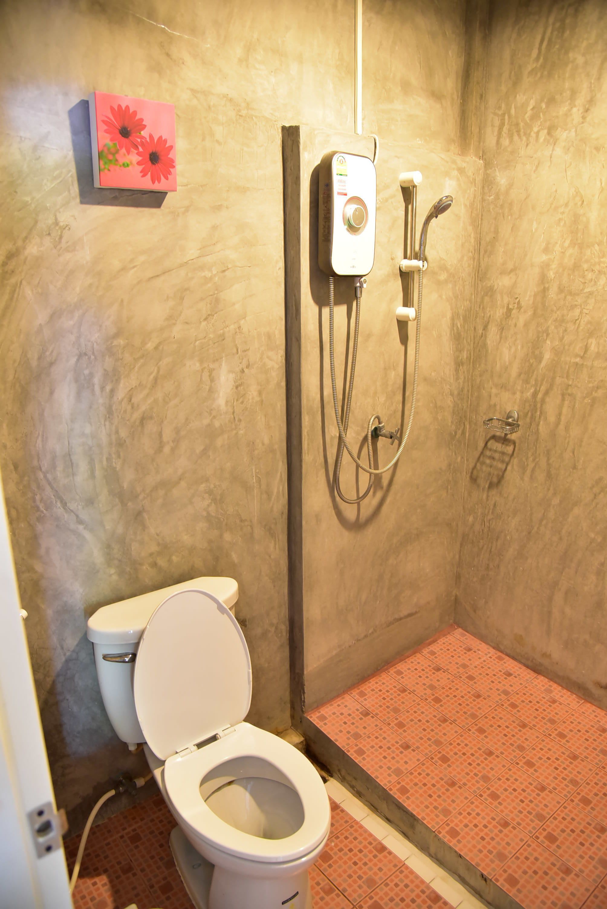 A bathroom with a toilet, a shower with a handheld showerhead, and a wall-mounted control panel.