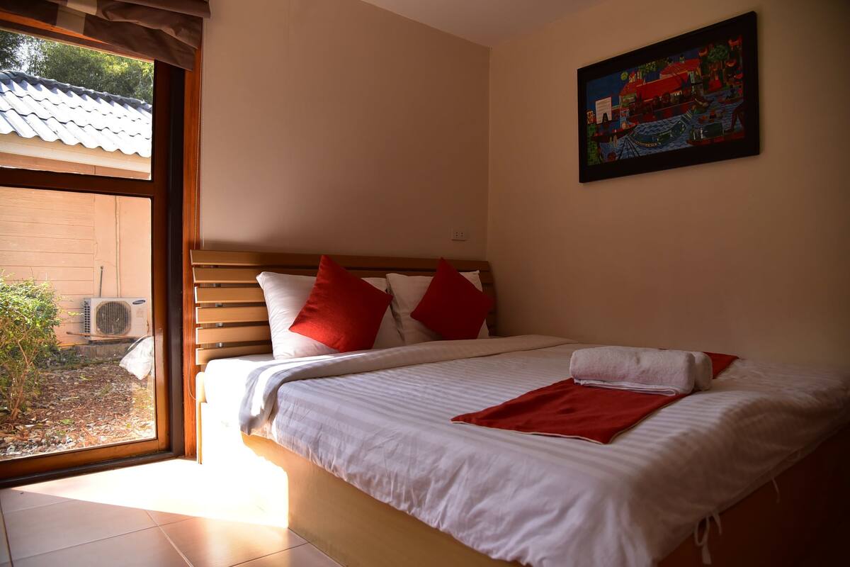 Un dormitorio con cama, almohadas, un cuadro y una ventana con vistas al exterior.
