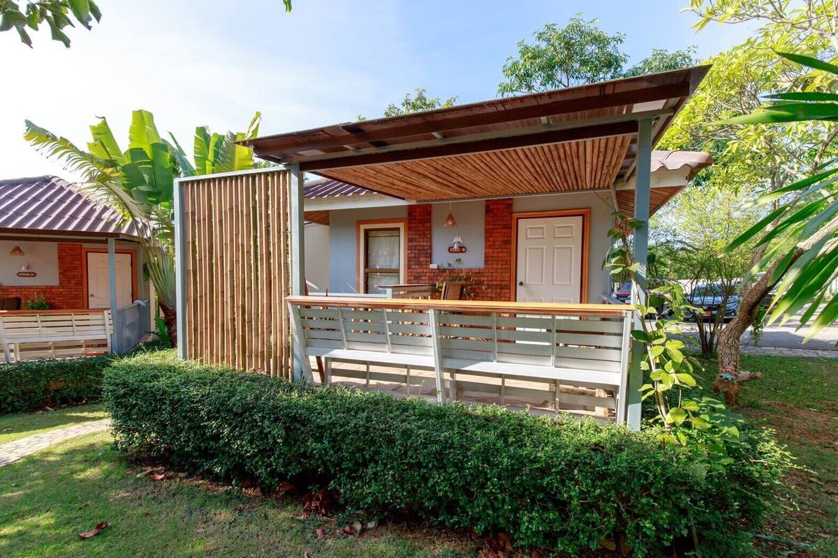 Un espacio de estar techado al aire libre con un banco, cerca de madera y un edificio con pared de ladrillo y puerta.