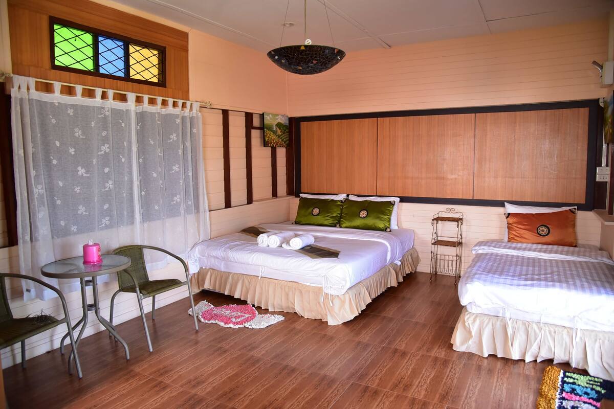 Habitación de hotel con dos camas, una mesita, sillas, un ventanal con vidrieras y un cabecero de madera.