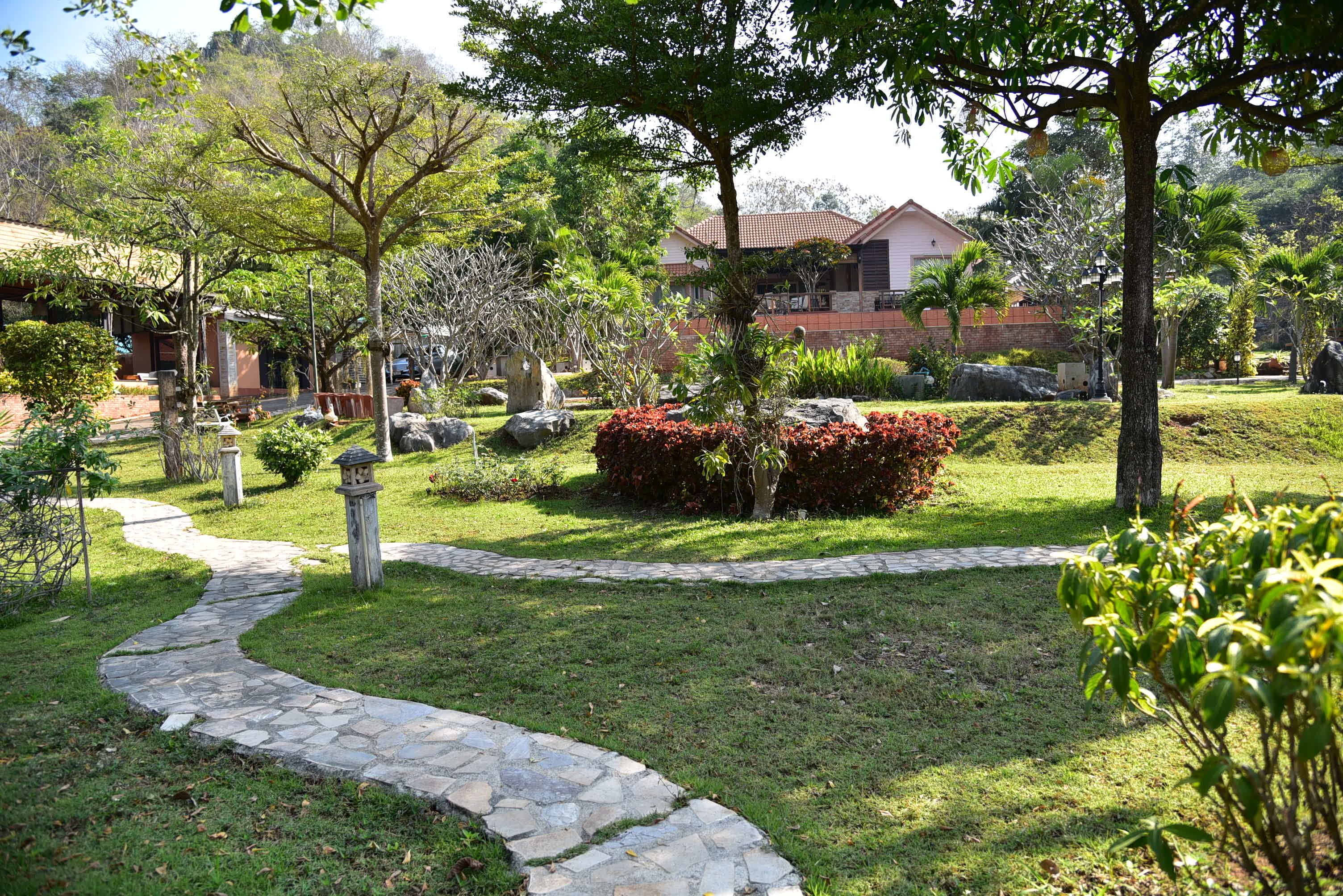 A landscaped garden with a stone pathway, various shrubs, and a building in the background.