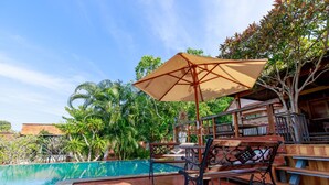 Zona de piscina amb una banca de fusta, una taula i un parasol gran.