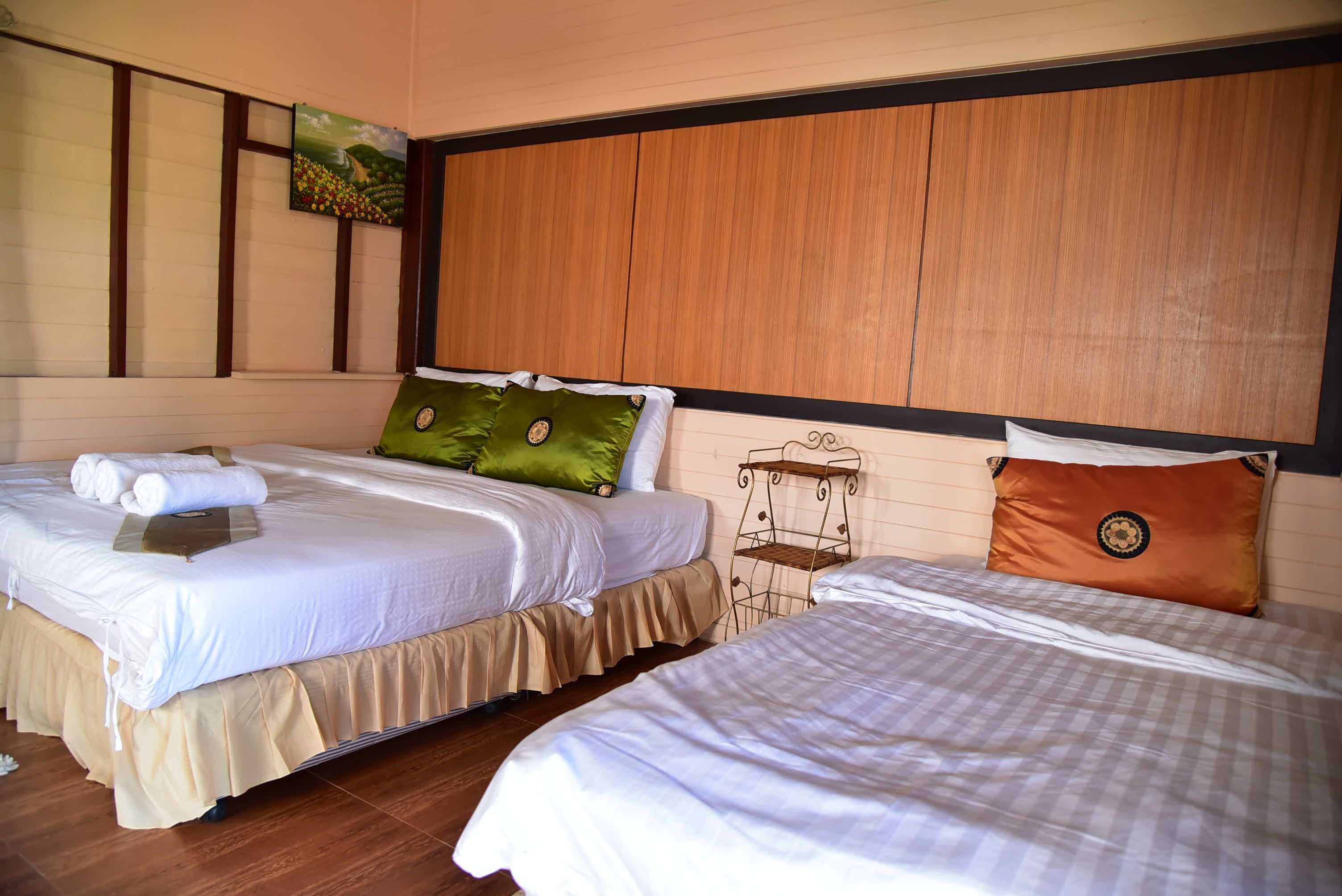Habitación de hotel con dos camas, cabecero de madera, un cuadro y una pequeña estantería.