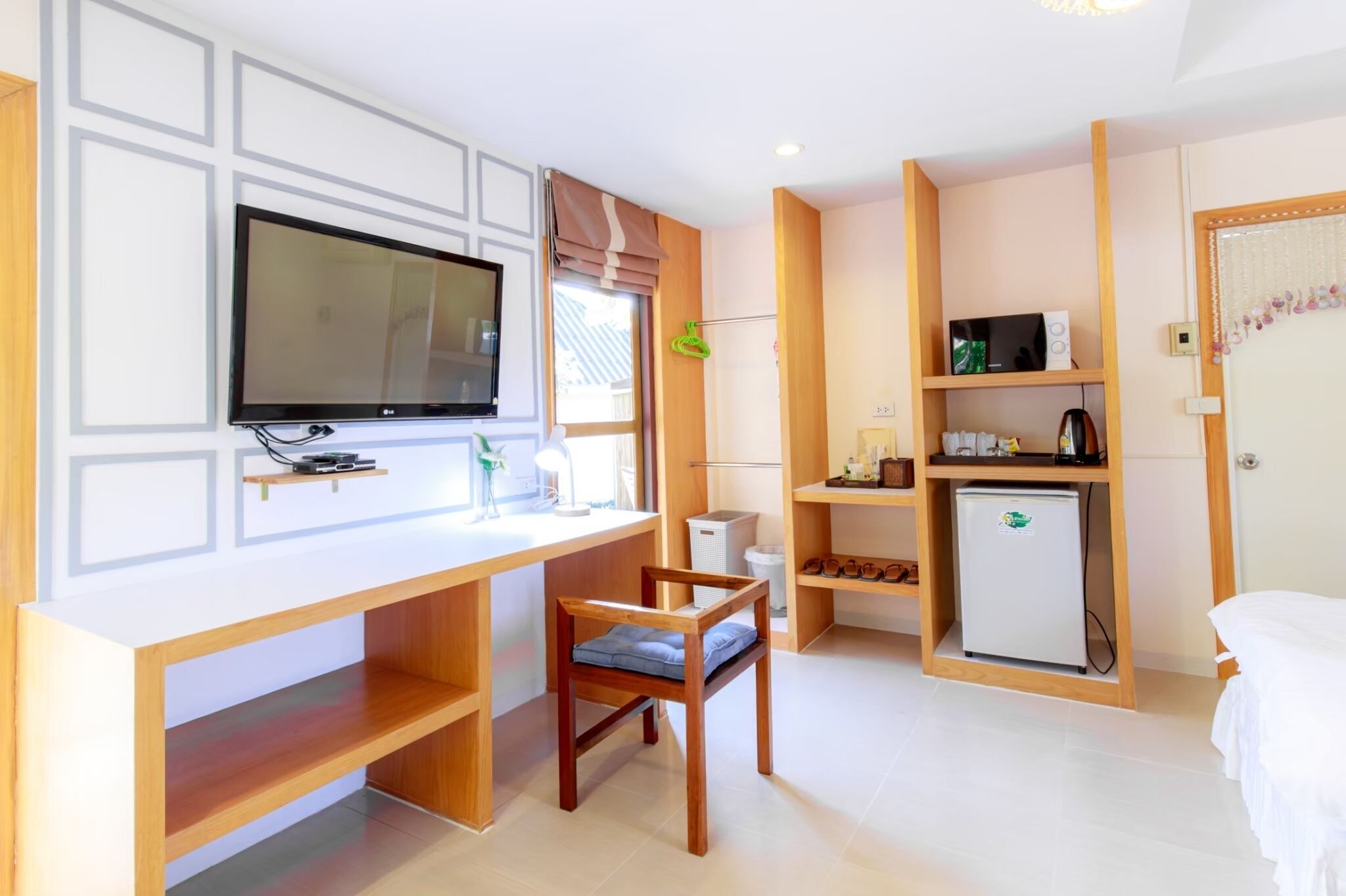 A hotel room with a wooden desk, a television, a small refrigerator, and a bed.