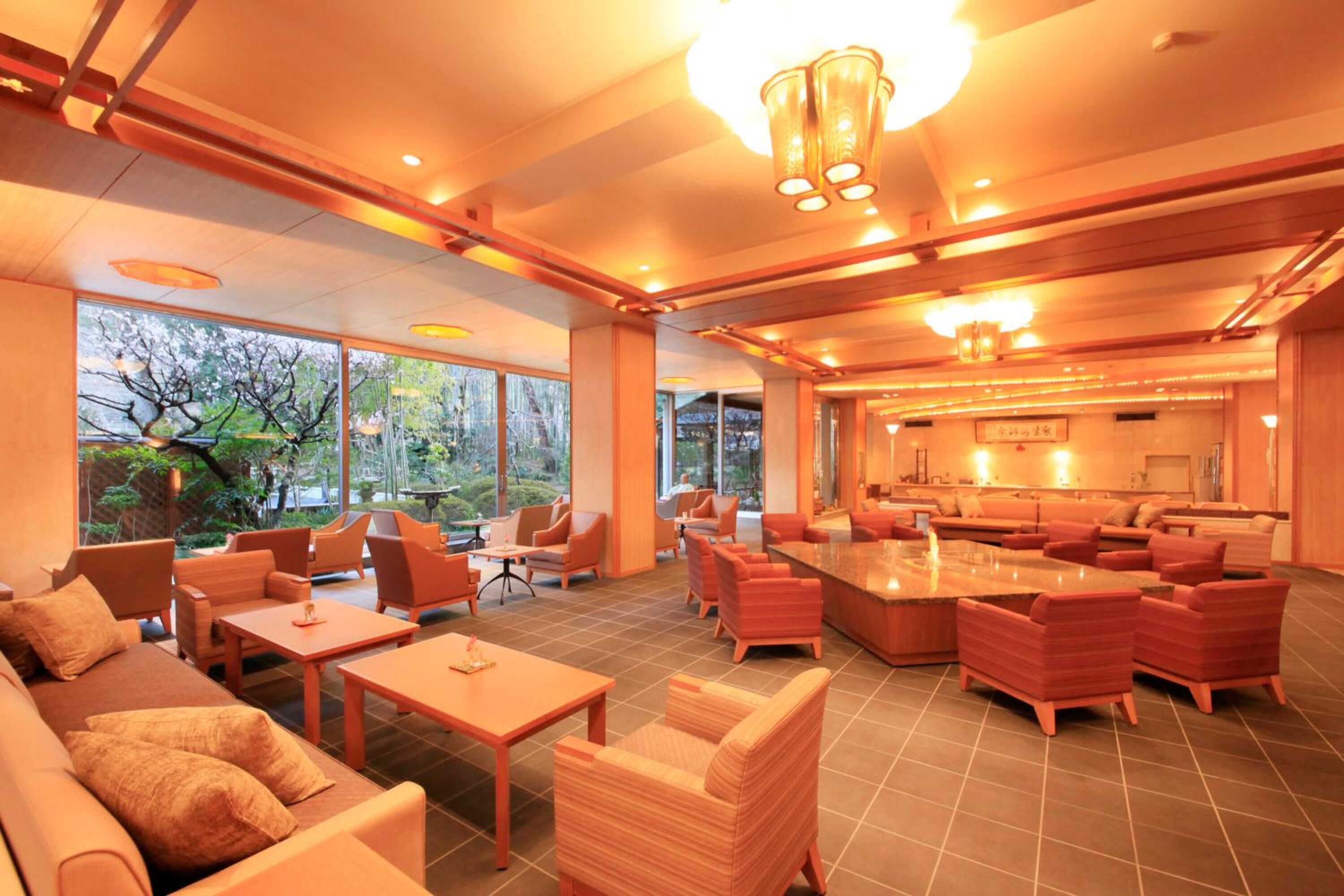 A spacious lounge area with multiple seating options, a central coffee table, and large windows offering a view of greenery outside.