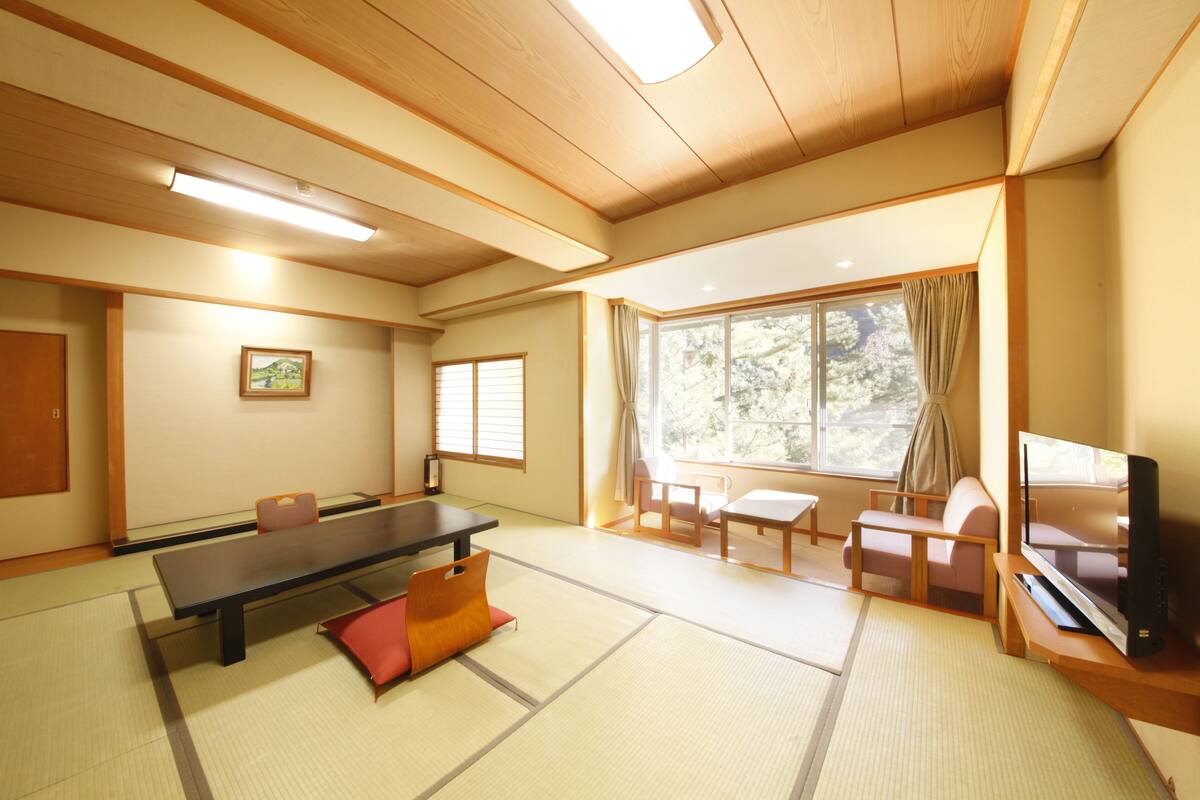 Una habitación de estilo japonés tradicional con suelo de tatami, una mesa baja, zona de estar y un televisor.
