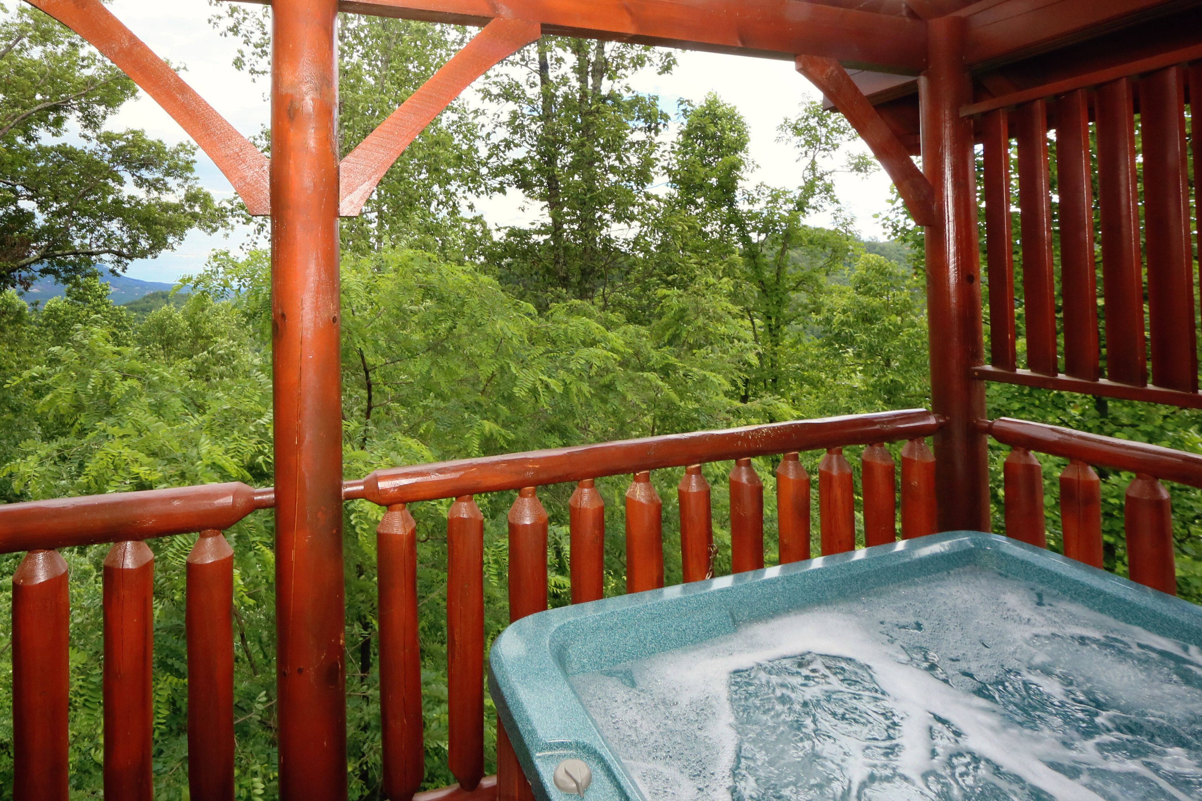 Une terrasse en bois avec un jacuzzi, entourée d’une végétation luxuriante et d’arbres.