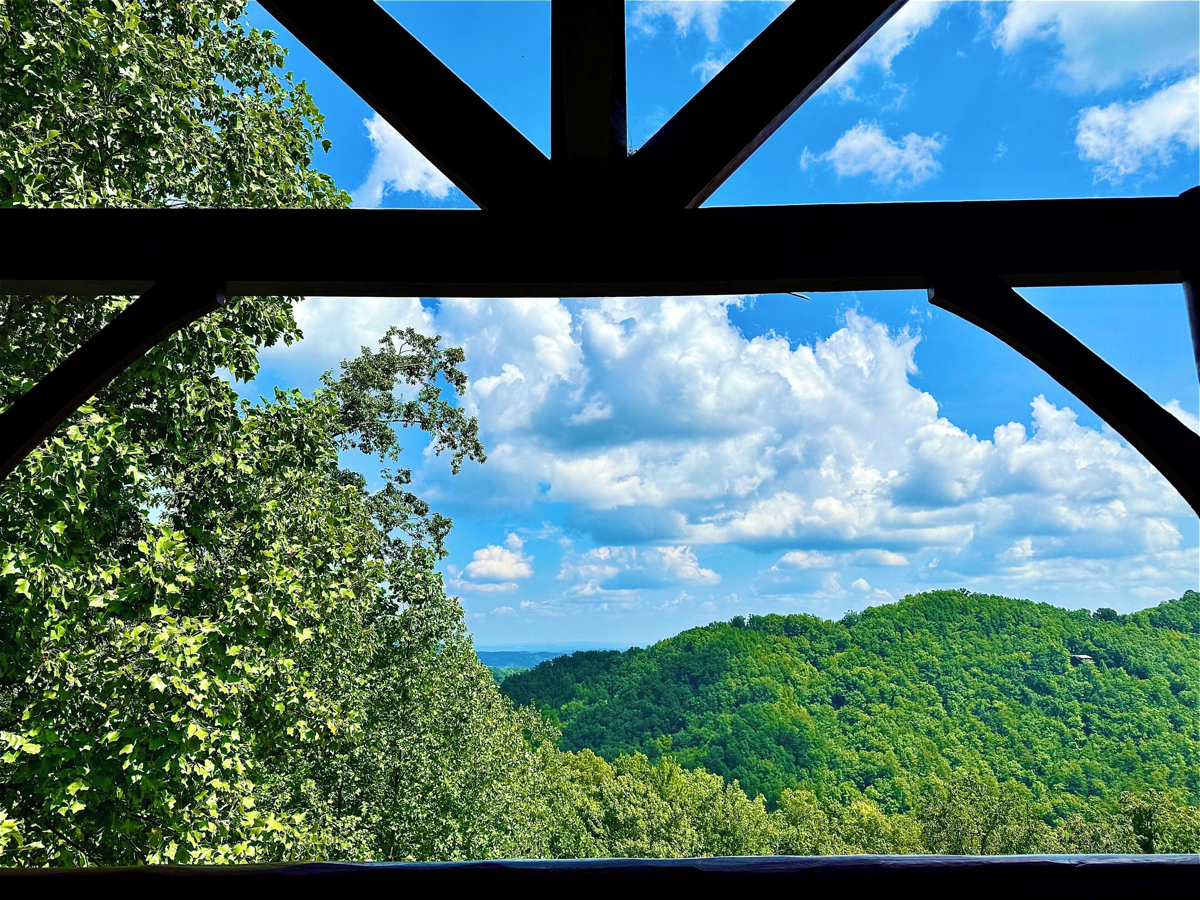 Vista a través de una estructura de madera, con un cielo despejado y colinas verdes exuberantes al fondo.