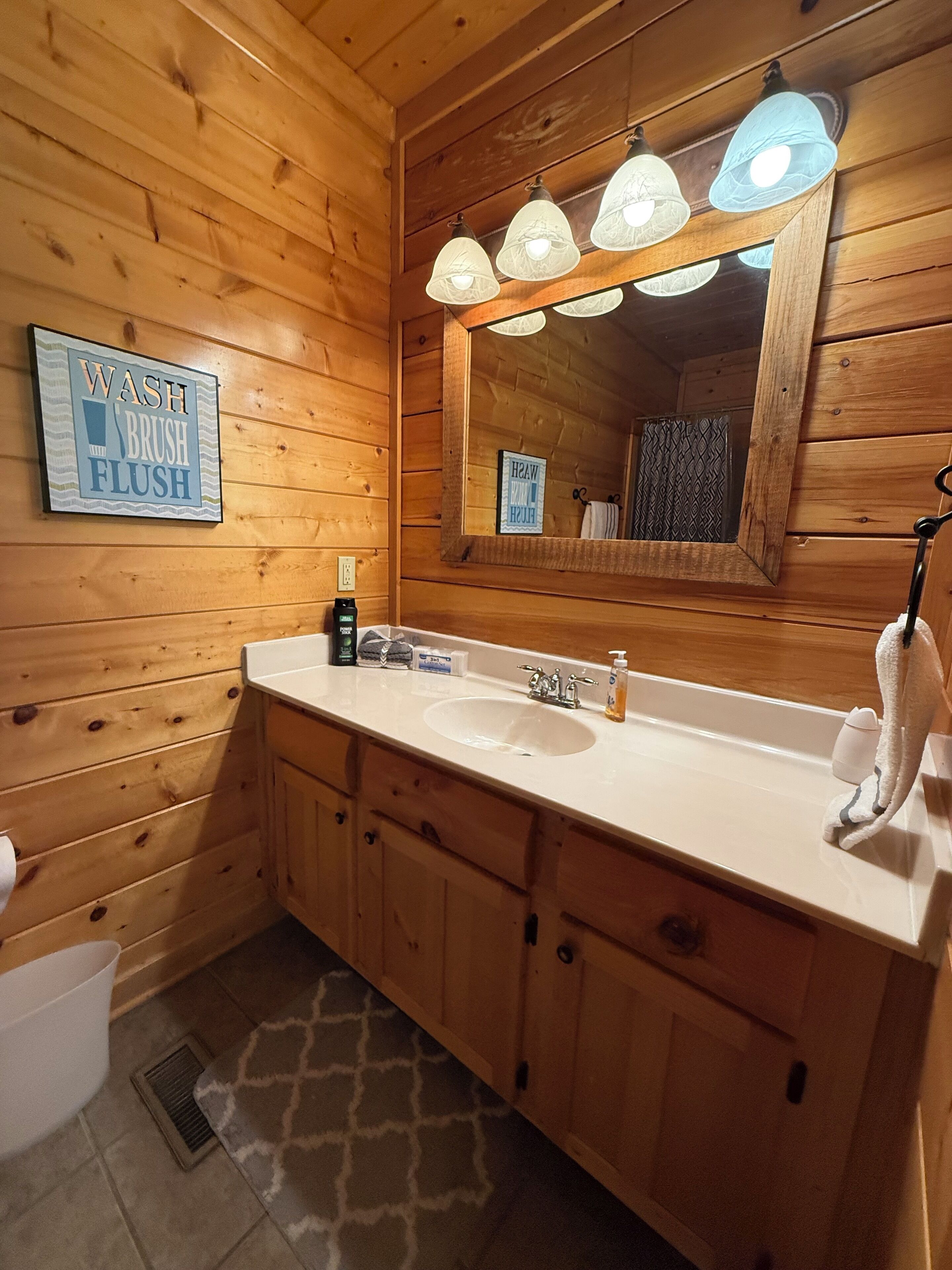 Een houten badkamer in een vakantiehuisje, met een wastafel, spiegel en een bord met de tekst 'WASH BRUSH FLUSH'.