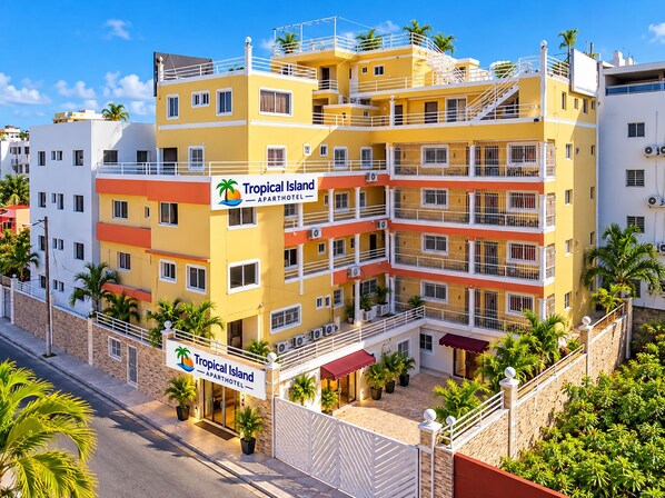A multi-story building with balconies and a sign indicating it is an apartment hotel named Tropical Island.
