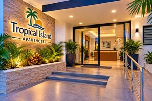 The entrance to Tropical Island Apartment Hotel with a reception desk, indoor plants, and a staircase leading to the interior.