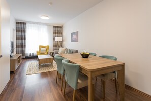 Ein modernes Wohnzimmer mit einem Holzesstisch, smaragdgrünen Stühlen, einer Couch und einem Fernseher.