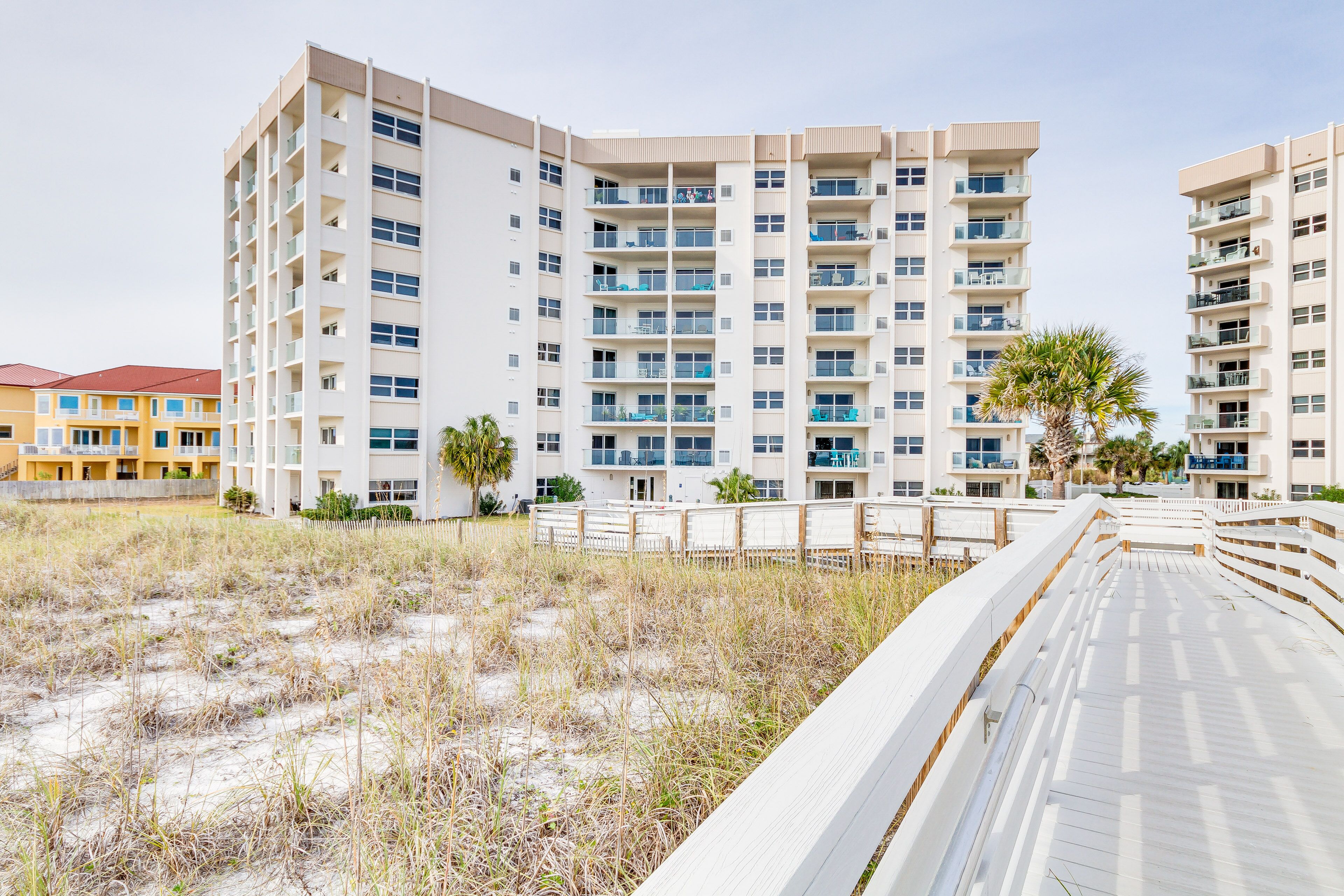 Ein Strandhotel mit mehreren Etagen, Balkonen und einer Promenade, die zum Strand führt.