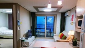 Quarto de hotel com cama, televisão, mesa de jantar com cadeiras, varanda com vista e uma pequena cozinha equipada.
