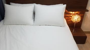 A neatly made bed with white linens and pillows, a wooden headboard, and a bedside table with a decorative lamp.