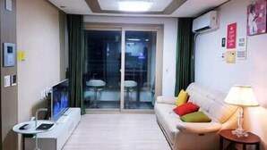 Sala de estar moderna com sofá, televisão e uma pequena mesa. Há uma porta de vidro deslizante que dá para uma varanda.