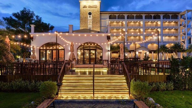 Un hotel con una torre central, varios balcones y una entrada iluminada con luces colgantes.