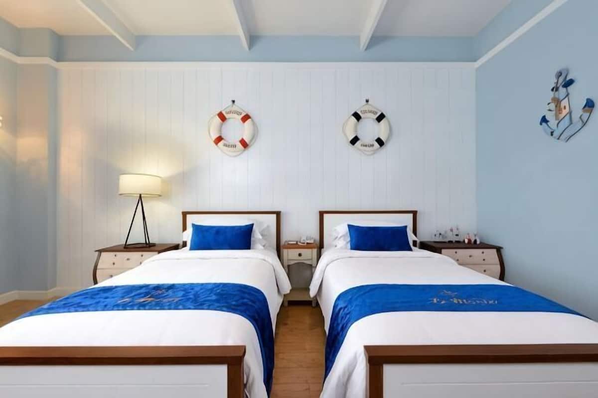 A hotel room with two beds, a nightstand with a lamp, and life rings on the wall.