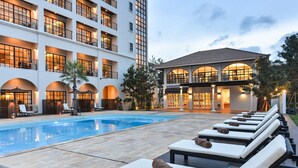 Un hotel con piscina, sillas de descanso y un edificio de varios pisos con balcones.
