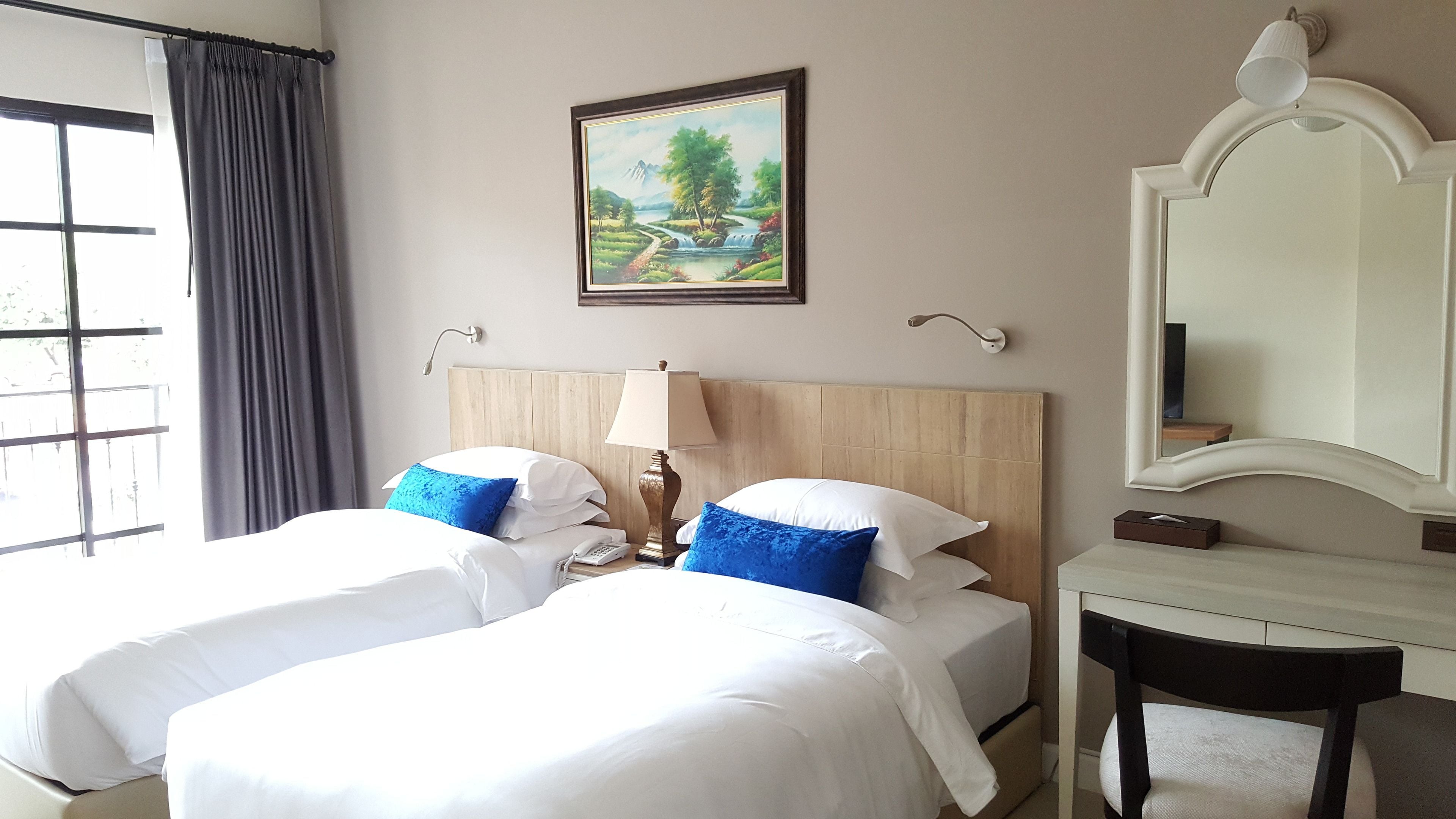 Habitación de hotel con dos camas, un cuadro, un escritorio y un espejo.