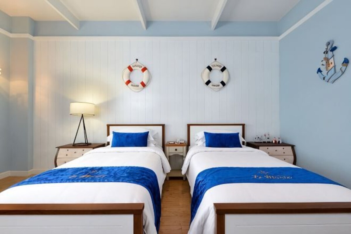 A hotel room with two beds, a nightstand with a lamp, and life rings on the wall.