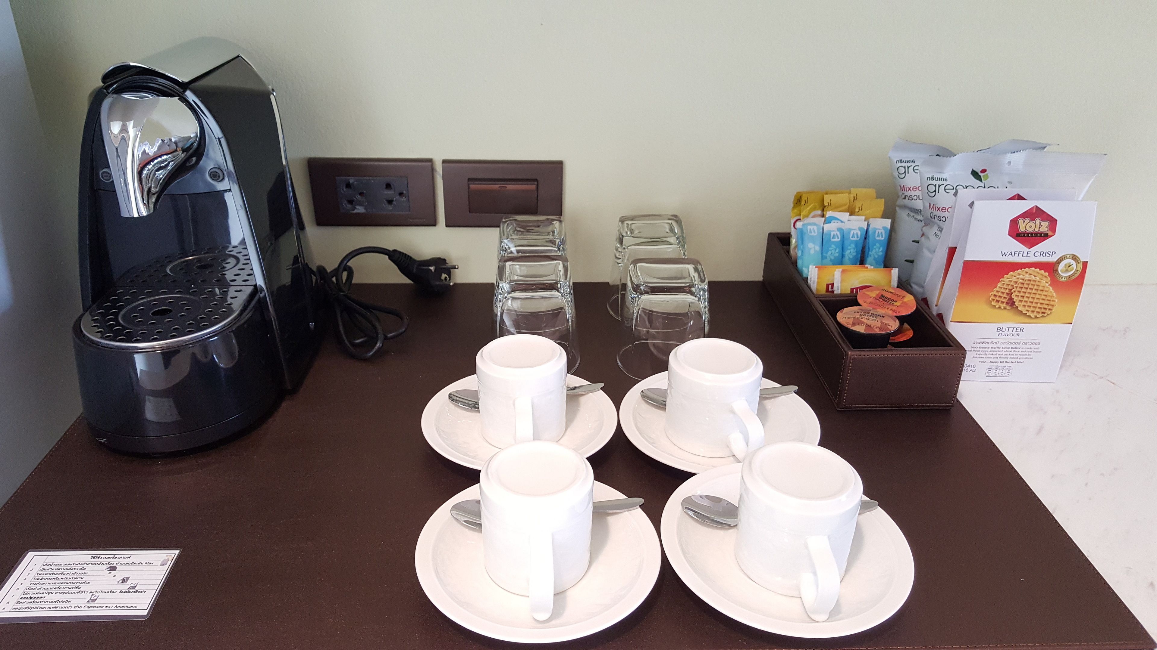 A breakfast setup with a coffee maker, cups, saucers, and a box of waffle crisps.