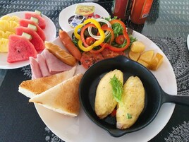 Un plato de desayuno con tostadas, jamón, sandía, pimientos y una sartén con huevos.