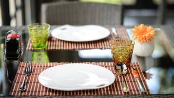 A dining table set with plates, cutlery, and glasses, with a decorative orange flower in a vase.