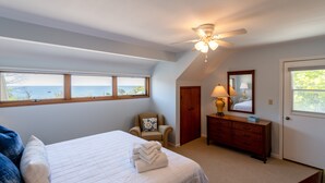 Une chambre à coucher comprenant un lit, une chaise, une commode, un ventilateur de plafond et une fenêtre donnant sur l’océan.