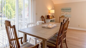 Un espace repas avec une table en bois, des chaises à rayures et une vue sur l’extérieur grâce à de grandes fenêtres.