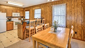 Una cocina con armarios de madera, un microondas y una zona de comedor con mesa y sillas de madera.