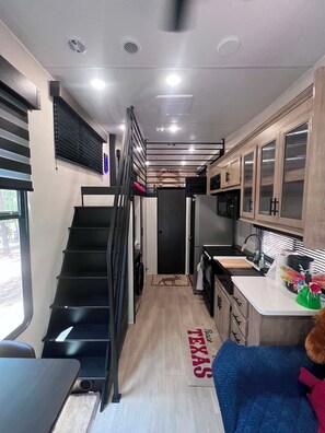Una cocina compacta con una escalera central, armarios de madera y un pequeño rincón de estar.