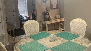 A dining room with a round table, four chairs, and a chandelier. There is a window with blinds, a door, and a wall-mounted sign. - Cozy, comfortable and convenient (Pensacola)