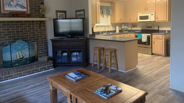 A modern kitchen with a central island, a dining area with a wooden table, and a TV on a cabinet. - Cozy, comfortable and convenient (Pensacola)