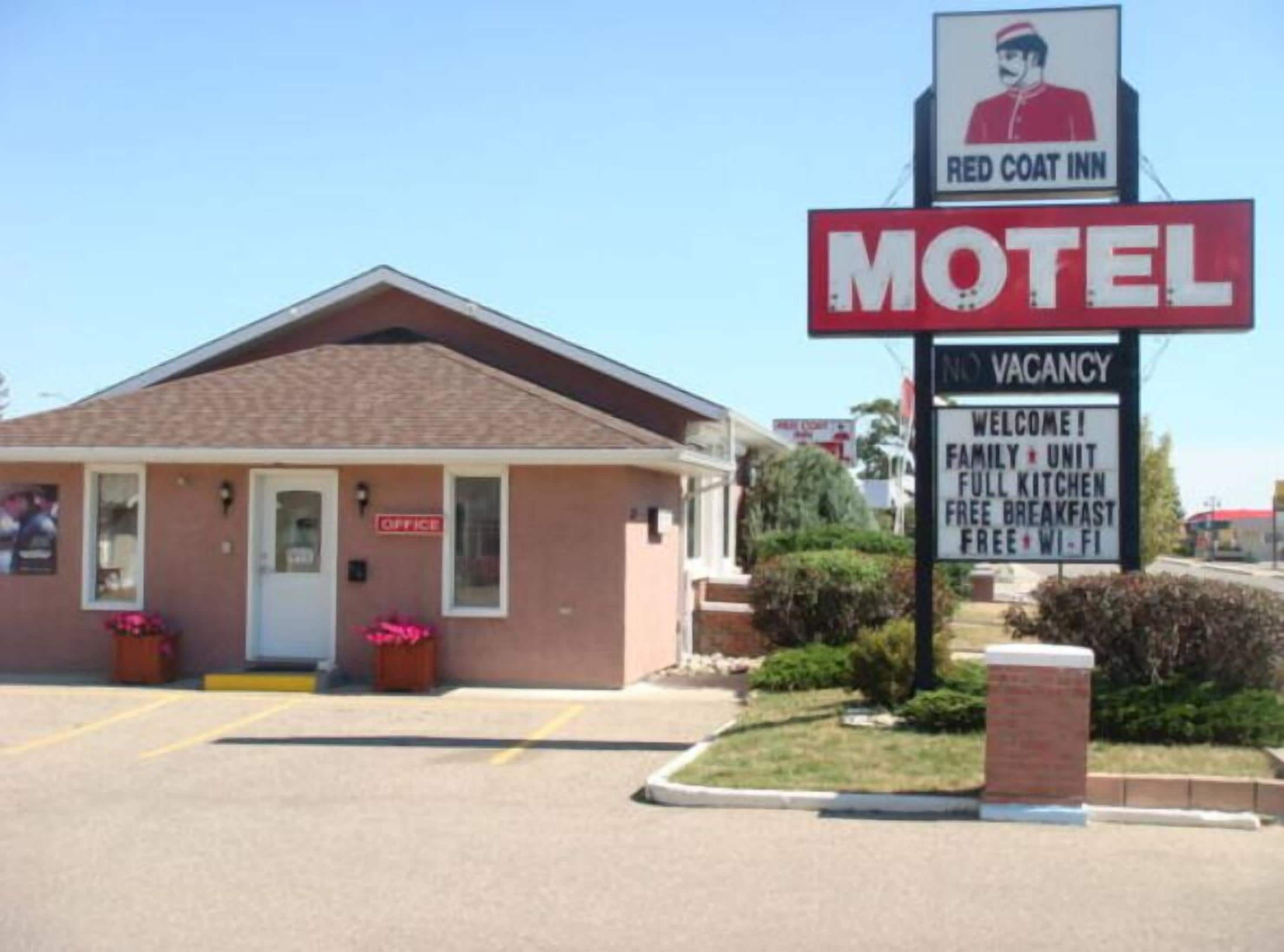 A motel with a 'VACANCY' sign, a 'RED COAT INN' sign, and a welcome sign advertising a family unit, full kitchen, free breakfast, and free Wi-Fi.