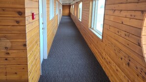 A corridor with wooden walls, carpeted floor, and windows along one side. - Red Coat Inn (Fort Macleod)