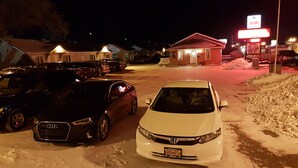 A parking lot with several cars, including an Audi and a Honda, parked in front of a building with a sign that reads "Welcome!" and "No Smoking." - Red Coat Inn (Fort Macleod)