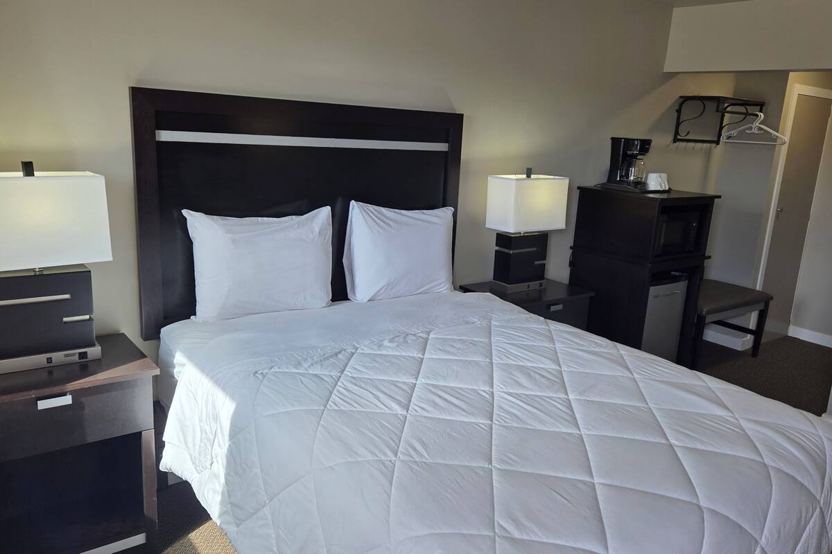 A hotel room with a bed, two bedside tables with lamps, a desk with a coffee maker, and a chair.