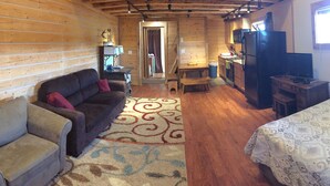A cozy cabin interior with a sofa, a bed, a dining table, and a kitchen area. - Authentic Fairbanks log house with bathroom, kitchen, and screened front porch (Fairbanks)