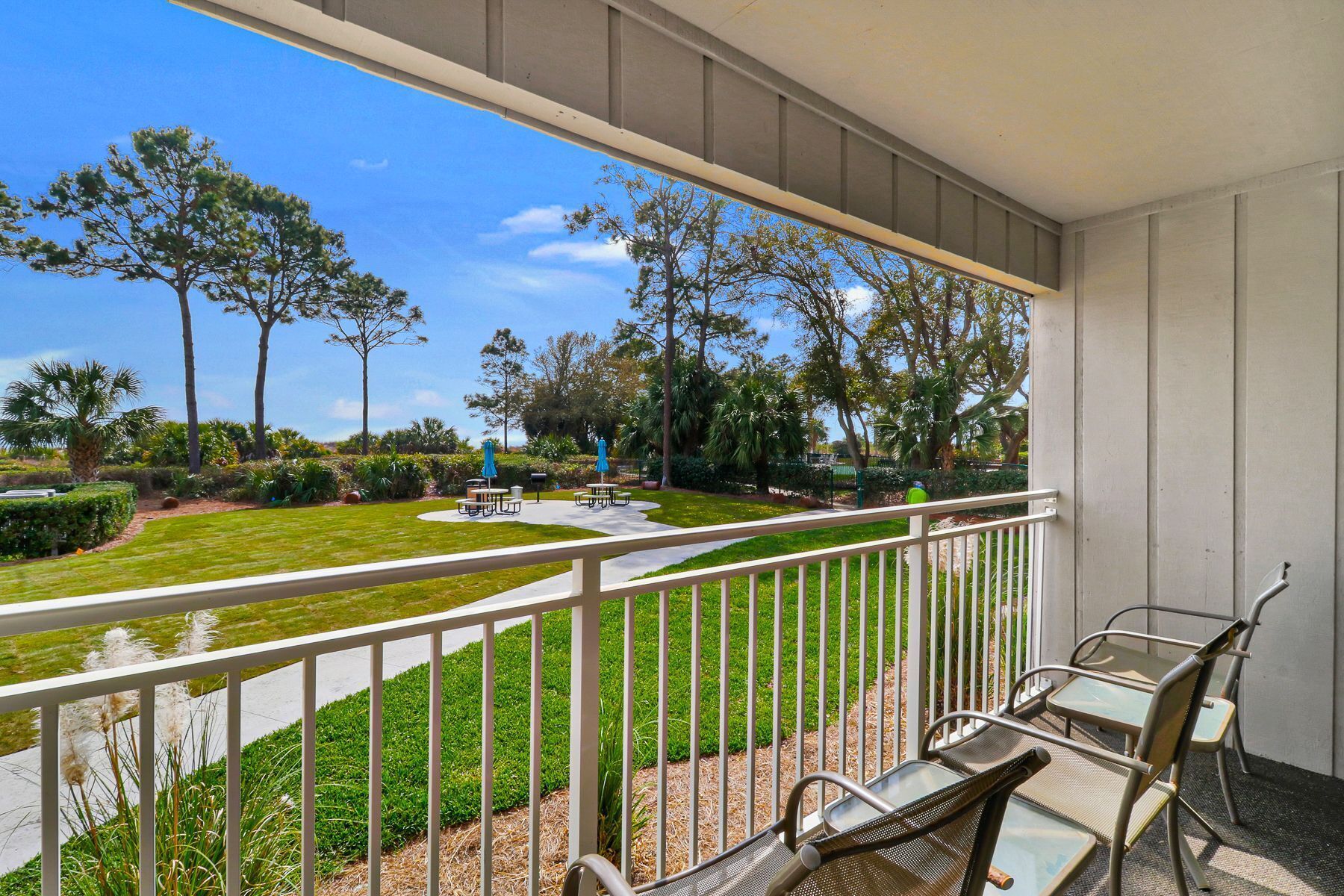 A balcony with a view of a well-maintained lawn and trees, outdoor furniture, and a clear sky.