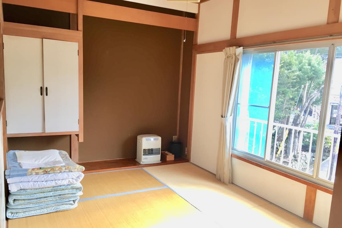 A room with tatami mat flooring, a heater, a wardrobe, and a window with a view of trees.
