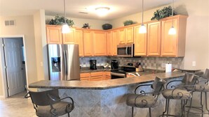 A kitchen with wooden cabinets, stainless steel appliances, a granite countertop, and bar stools.