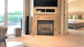 A living room with a fireplace, a flat-screen TV mounted above it, and a large sliding glass door leading to a balcony.