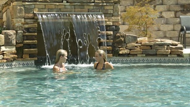 A pool with a waterfall feature and stone walls.