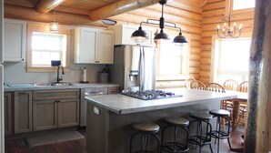 A kitchen with wooden walls, a central island with stools, a refrigerator, and pendant lighting.