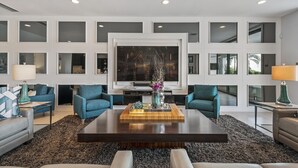 A modern living room with a large flat-screen TV, two blue armchairs, a grey sofa, a wooden coffee table, and a decorative vase. - Modern Estate | 8,400 sq ft Luxury Villa with Games Room, Private Pool & Spa (Kissimmee)