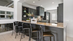 A modern kitchen with a large island, black bar stools, and built-in cabinetry. - Modern Estate | 8,400 sq ft Luxury Villa with Games Room, Private Pool & Spa (Kissimmee)