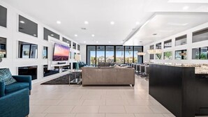 A spacious living area with a large TV, comfortable seating, and a view of the cityscape through large windows. - Modern Estate | 8,400 sq ft Luxury Villa with Games Room, Private Pool & Spa (Kissimmee)