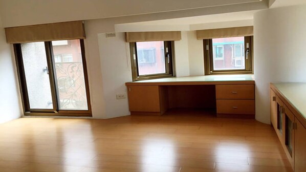 A room with a wooden desk, two windows with blinds, and a sliding glass door.