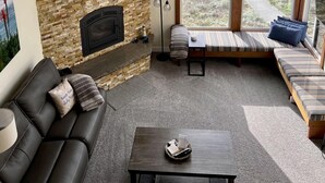 Ein Wohnzimmer mit Kamin aus Stein, einer Couch, einem Couchtisch und Meerblick durch große Fenster.